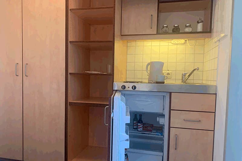 Küchenzeile mit Spüle, Wasserkocher, offenem Kühlschrank und Schrankregalen.