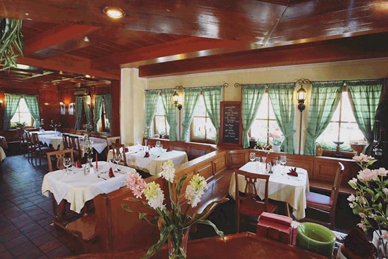 Restaurant mit Holzbänken, weiß gedeckten Tischen und grünen karierten Vorhängen.