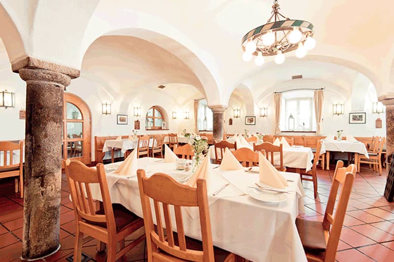 Gedeckter Gastraum mit gewölbter Decke, Steinpfeilern, Holztischen und weißen Tischdecken.