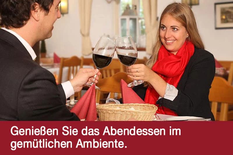 Paar stößt mit Rotwein an einem gedeckten Restauranttisch an.