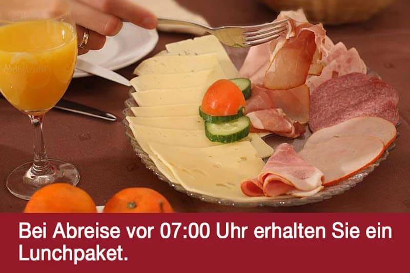 Teller mit Käsescheiben, verschiedenen Aufschnitten, Gurken-Tomaten-Garnitur und Glas Orangensaft.