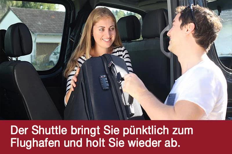 Mann reicht einer Frau im Fahrzeug einen Koffer, beide lächeln.